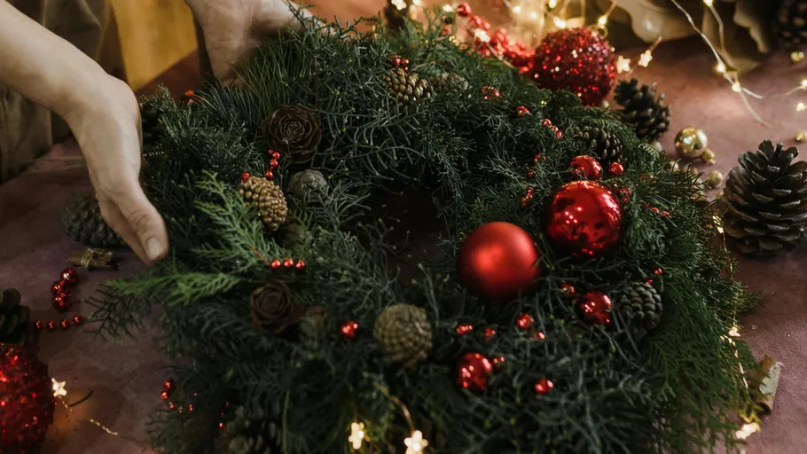 Hands holding decorated Christmas wreath indoors.