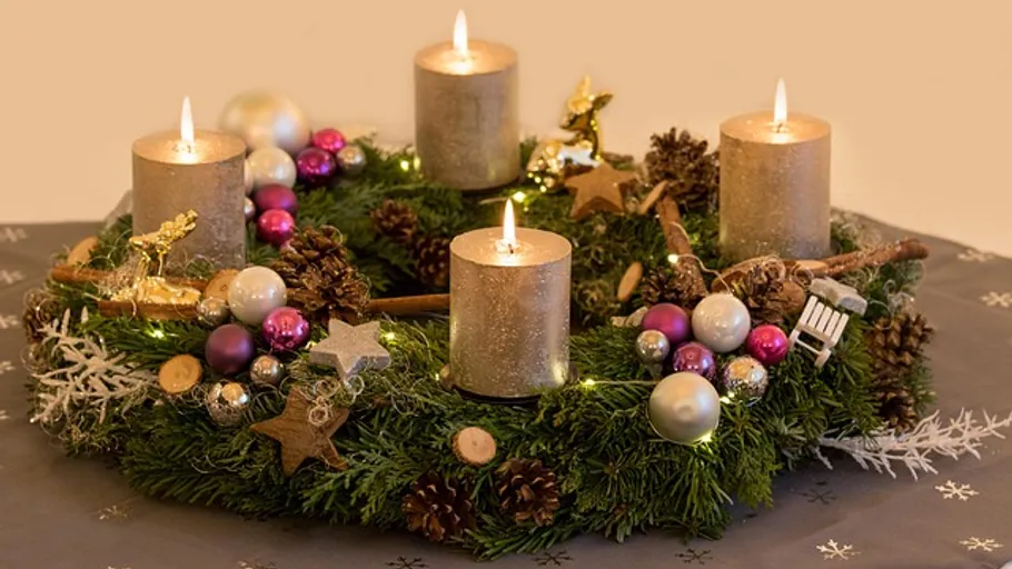 Adventskranz mit brennenden Kerzen auf Tisch.