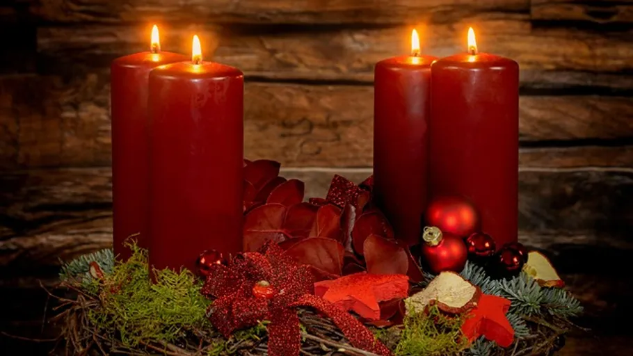 Four red candles on decorative wreath indoors.