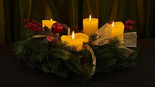 Candles lit on decorated evergreen wreath.