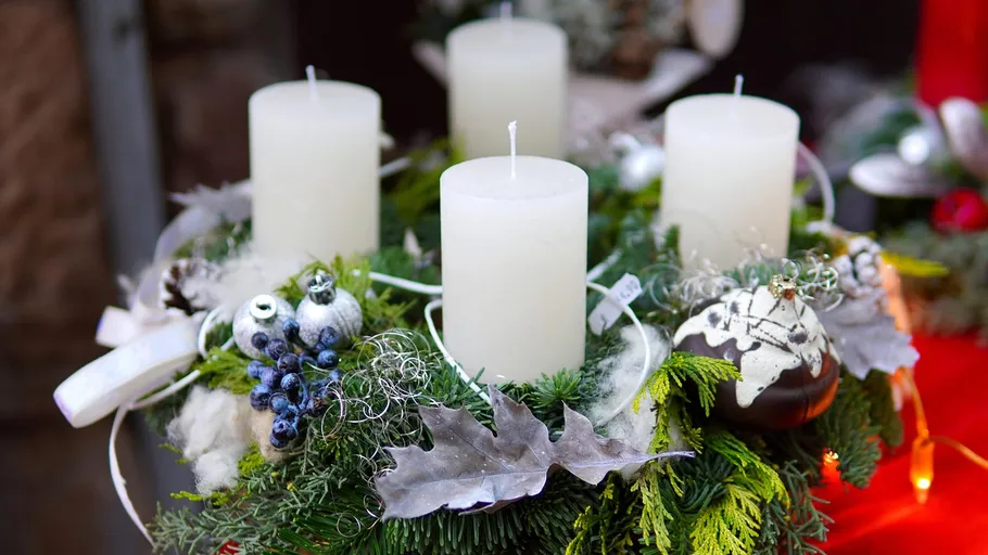 Vier weiße Kerzen auf dekoriertem Adventskranz.