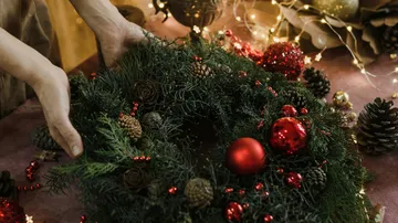 Hands arranging festive wreath with red ornaments.