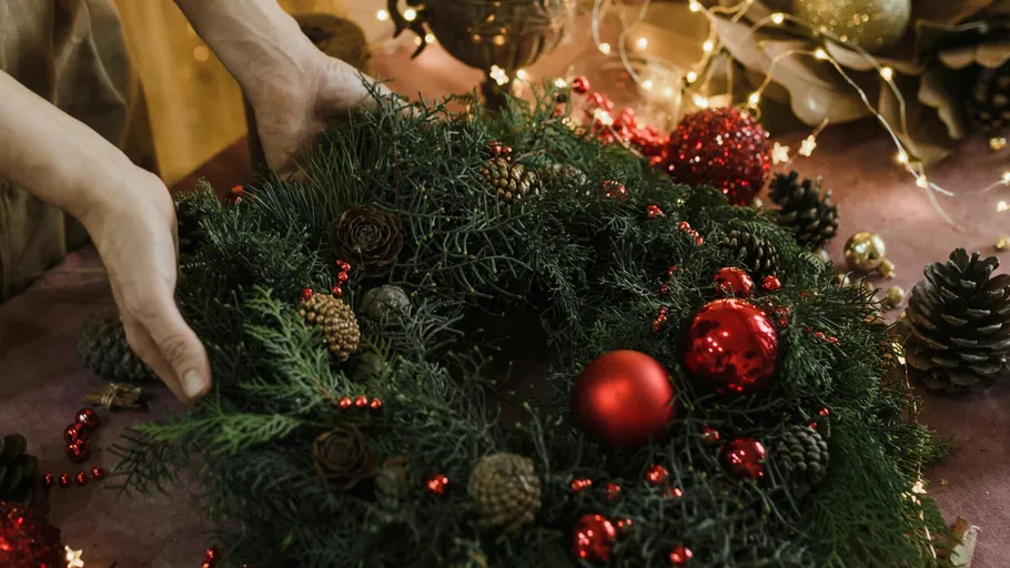 Hände arrangieren festlichen Kranz mit roten Ornamenten.