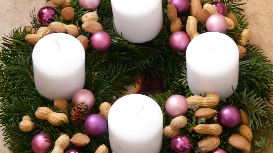 Vier Kerzen auf dekoriertem Adventskranz.