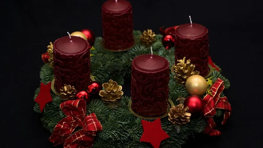 Advent wreath with four red candles on greenery.