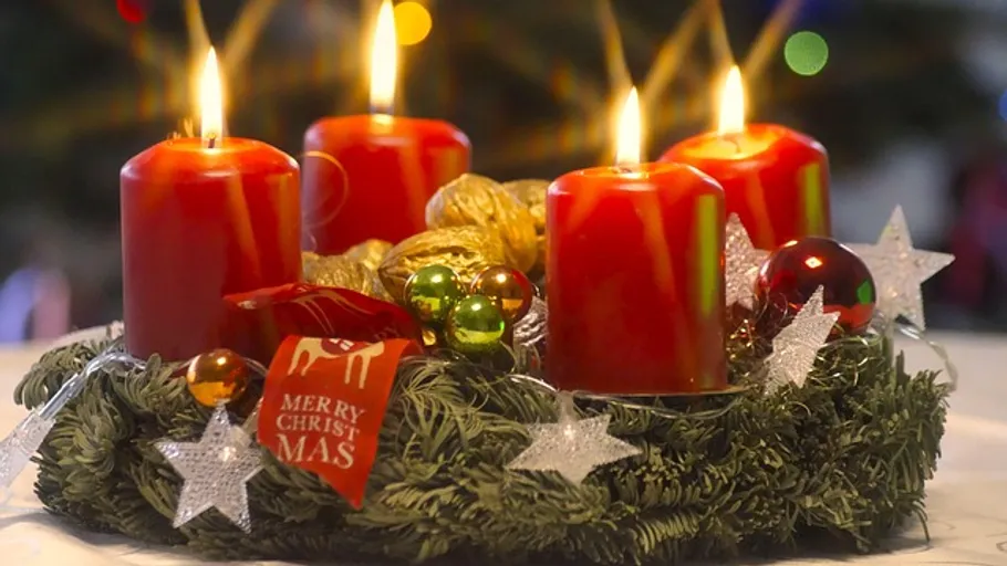Four lit candles on advent wreath, festive background.