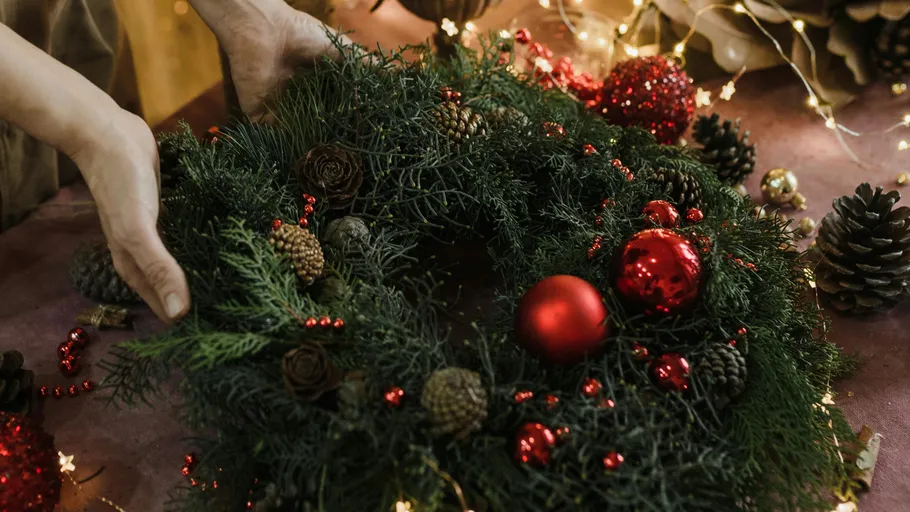 Hands arranging Christmas wreath with ornaments.