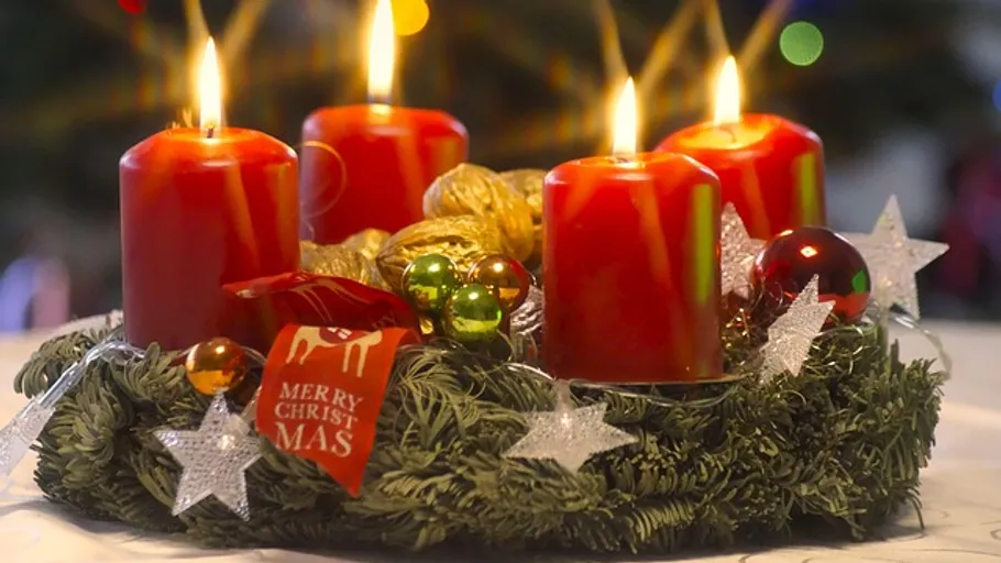 Four red candles lit on Christmas wreath.