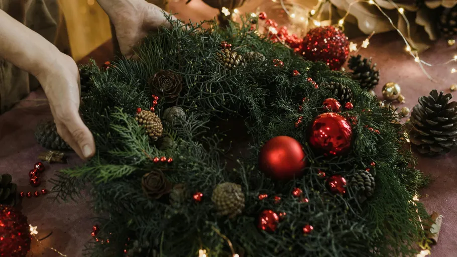 Hände arrangieren einen dekorierten Weihnachtskranz.