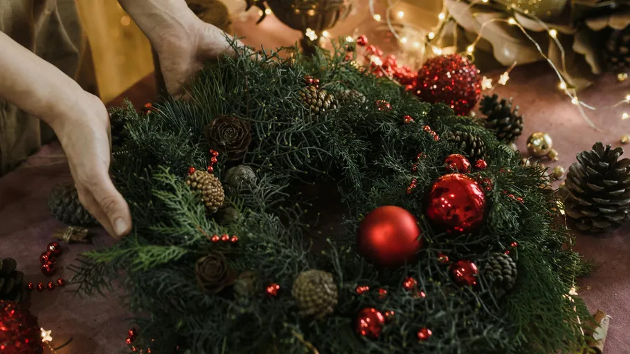 Hands arranging Christmas wreath with red ornaments.