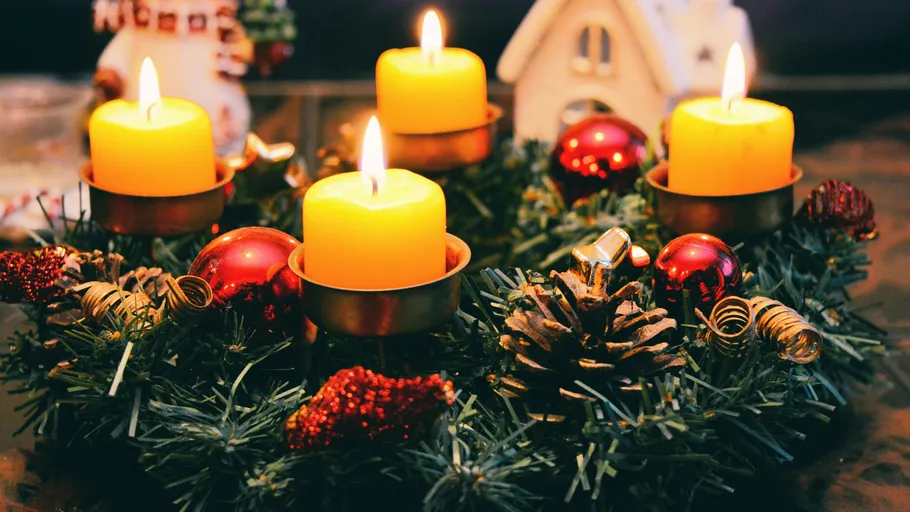 Vier brennende Kerzen auf geschmücktem Weihnachtskranz.