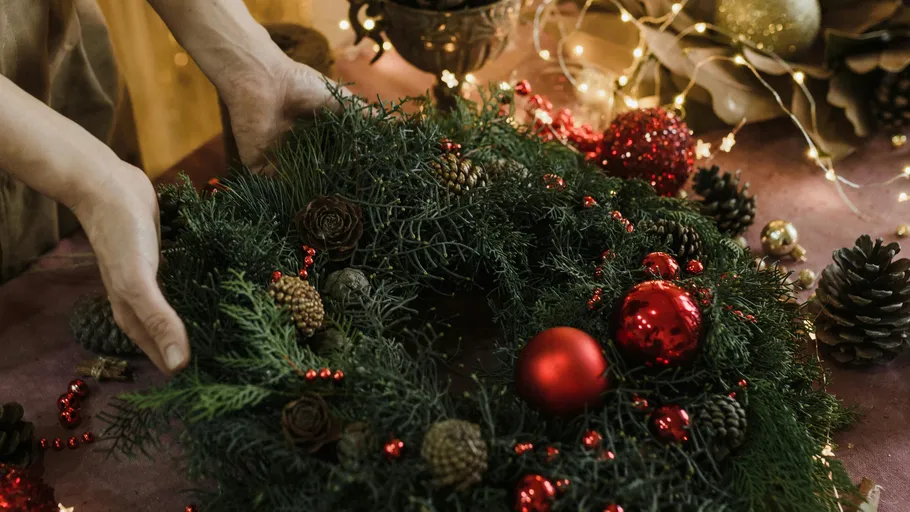 Hände arrangieren einen Weihnachtskranz mit Dekorationen.