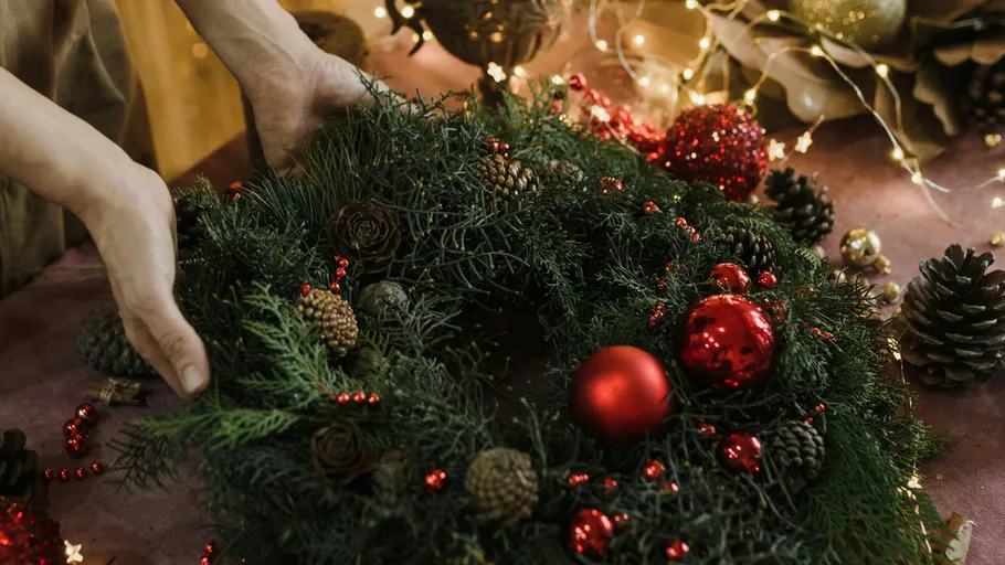 Hands arranging a festive wreath on table.