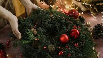 Hands arranging festive wreath with red ornaments.