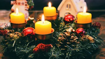 Vier Kerzen auf dekoriertem Adventskranz auf Tisch.