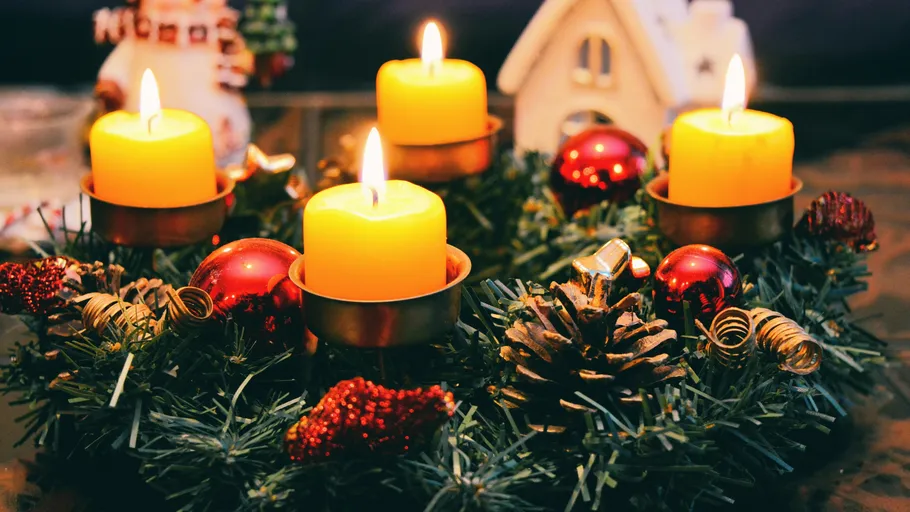 Four lit candles on decorated Christmas wreath.