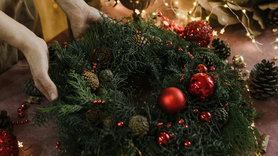Hände arrangieren einen Weihnachtskranz auf einem Tisch.