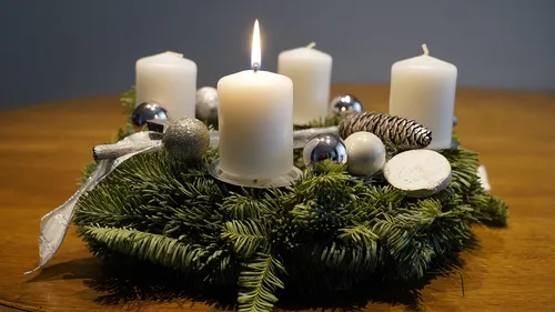 Adventskranz mit brennender Kerze auf Tisch.