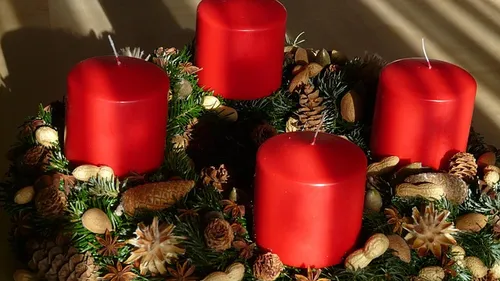 Rote Kerzen auf dekoriertem Adventskranz.