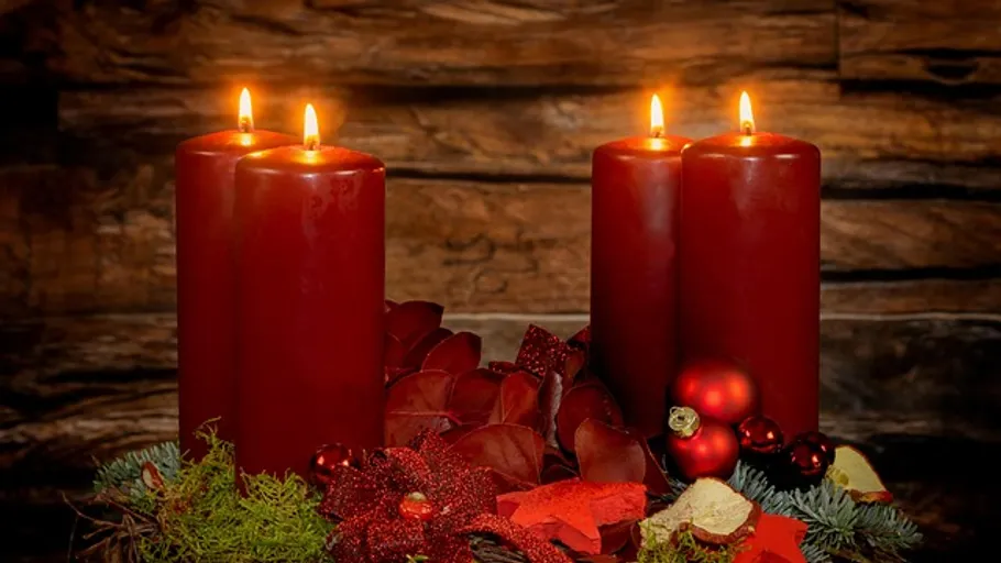 Four lit red candles on rustic background.