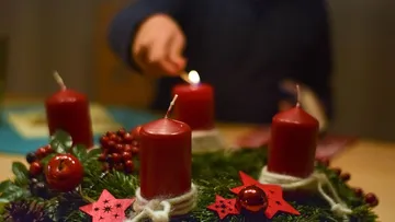 Red candles on wreath being lit indoors.