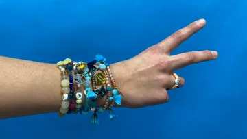 Arm with many bracelets making peace sign.