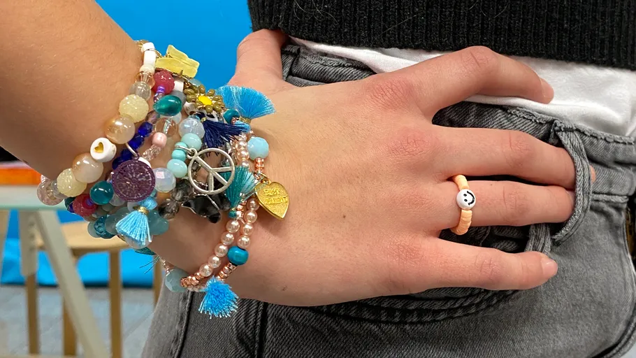 Hand with beaded bracelets, denim background.
