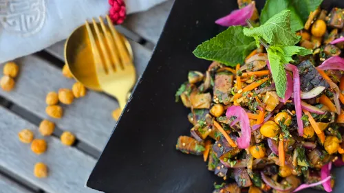 Bunter Kichererbsensalat auf schwarzem Teller, Holztisch.