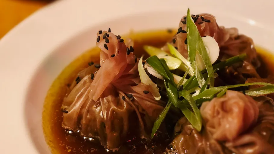 Dumplings in sauce with garnish on plate.