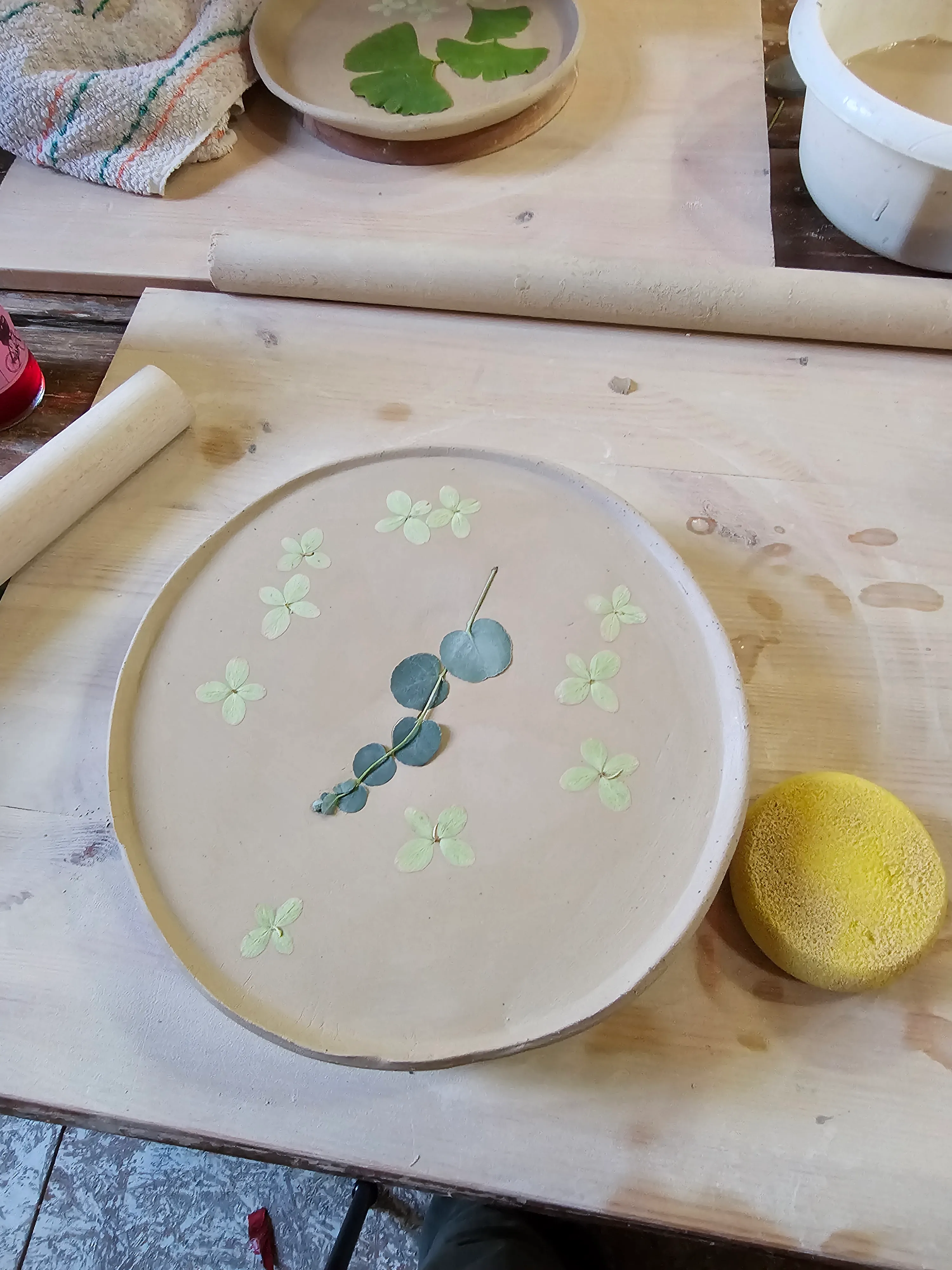 Clay plate with pressed leaves on wooden table.