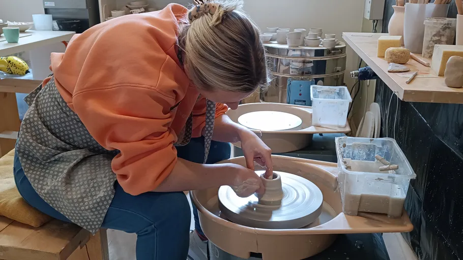 Woman shaping clay on a pottery wheel in workshop.