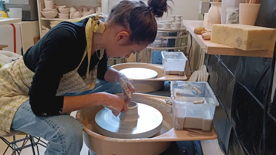Person shaping clay on pottery wheel indoors.