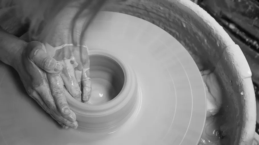 Hands shaping clay on pottery wheel.