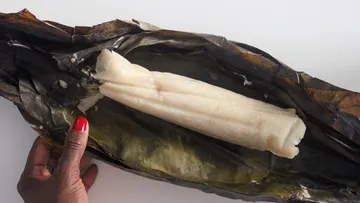 Hand unwrapping white dish in banana leaf.