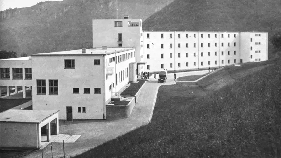 Large white building on hillside, several people outside.