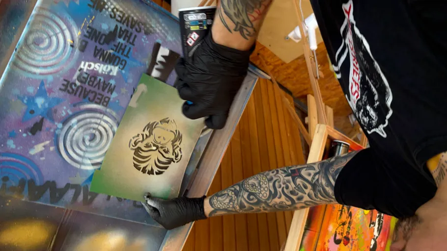 Tattooed artist stenciling colorful designs on a table.