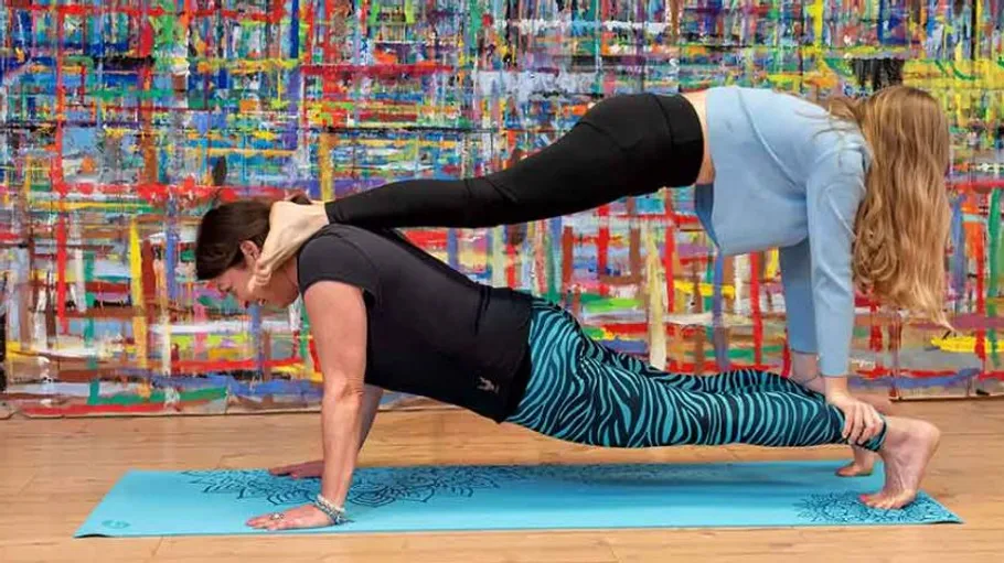 Two people performing acro yoga on a mat.