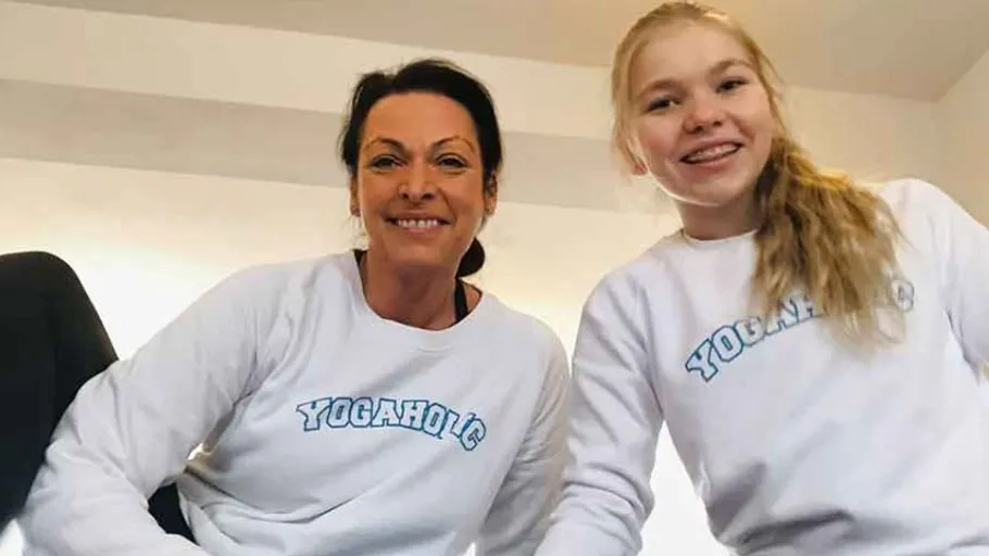 Zwei lächelnde Personen tragen 'Yogaholic'-Shirts drinnen.