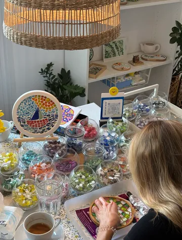 Woman making mosaic art at cluttered table.