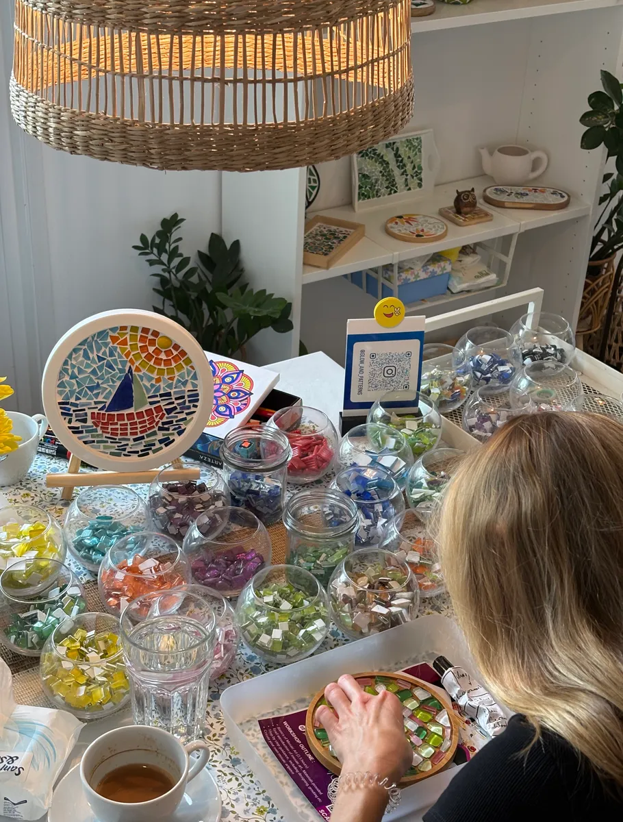 Woman making mosaic art at cluttered table.