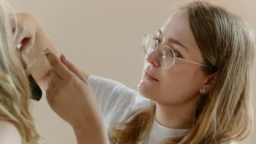 Woman wearing glasses styling someone's hair.