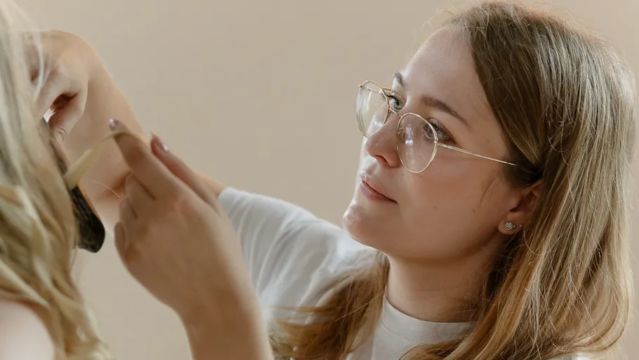 Frau mit Brille stylt jemandes Haare.