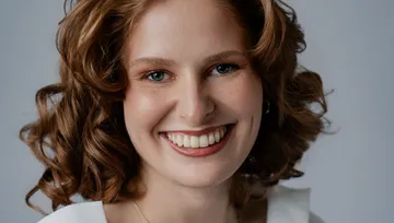 Lächelnde Frau mit lockigem Haar, weißer Hintergrund.