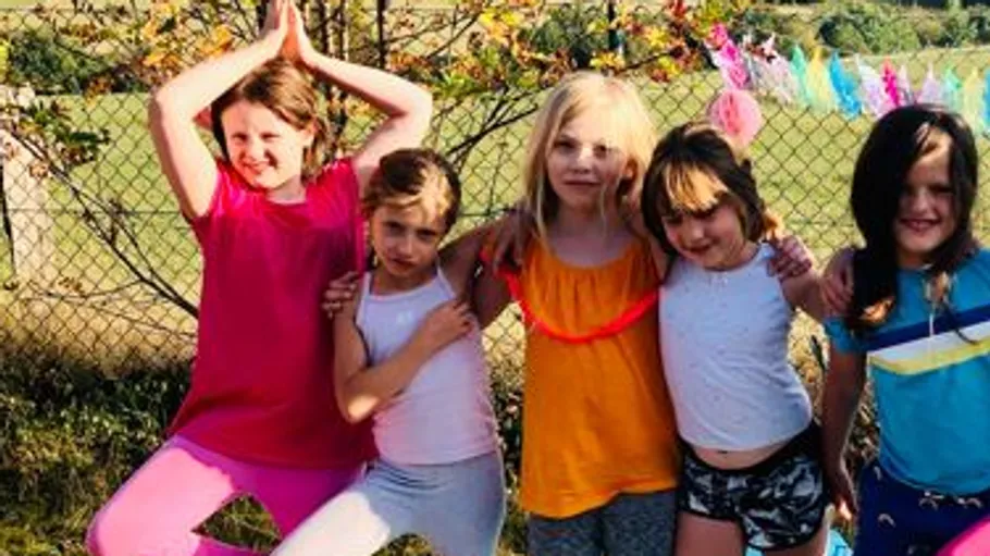 Fünf Kinder posieren in sonnigem Garten.