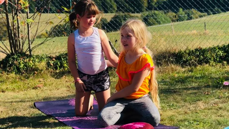 Zwei Mädchen sitzen auf Yogamatten im Freien.