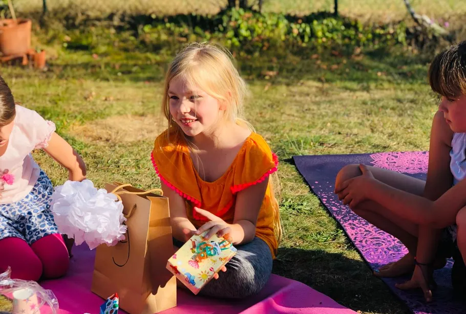 Kinder sitzen im Gras und öffnen Geschenke draußen.