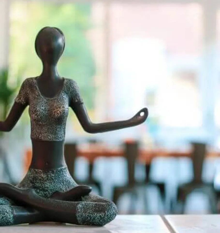 Sculpture of person meditating indoors.