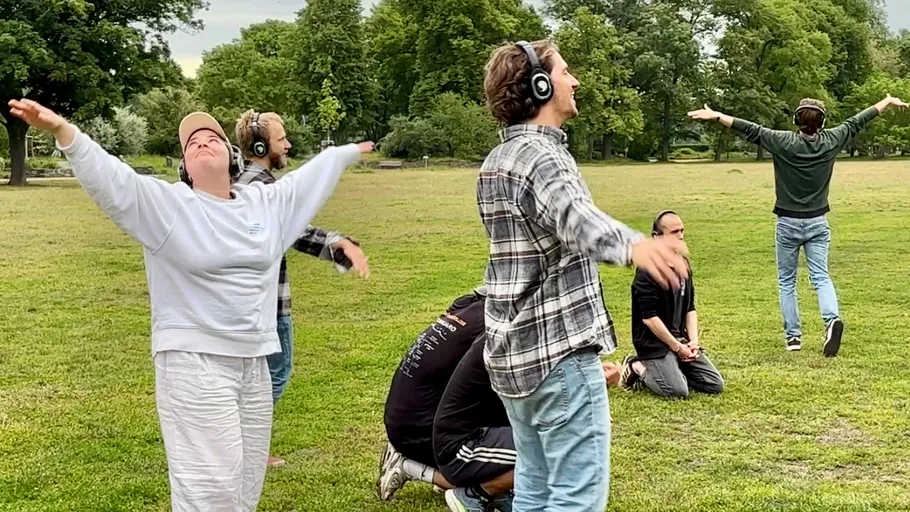 Personen mit Kopfhörern tanzen im Park.