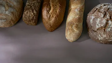 Fünf verschiedene Brote auf einer Tischoberfläche.