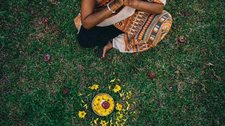 Person sitzt im Schneidersitz auf Gras mit Blumen.